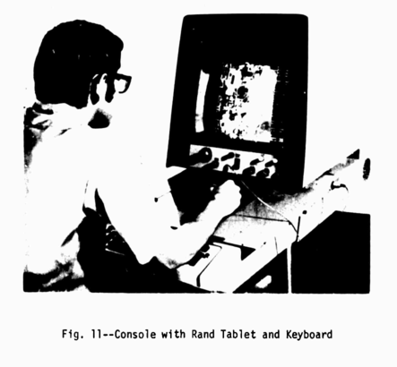 A blurry black and white image of a man hunched over an electronic tablet, looking at a monitor with a bunch of knobs and dials on it.