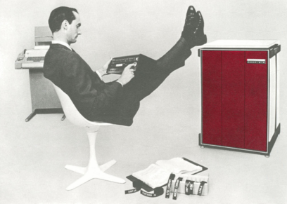 A man in a suit reclining in a space age chair with his feet up on the Honeywell DDP-516.